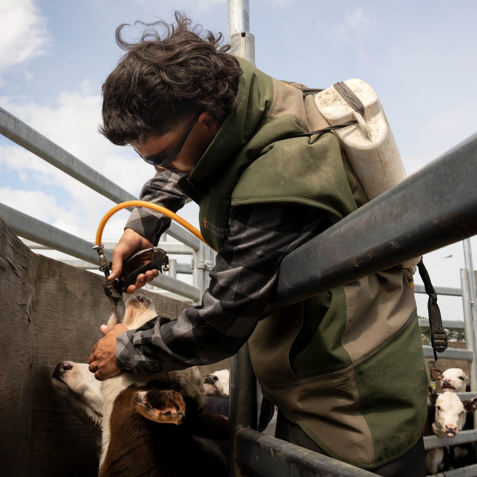 Person attending to a deer in a pen with a hose, wearing a green jacket and backpack.