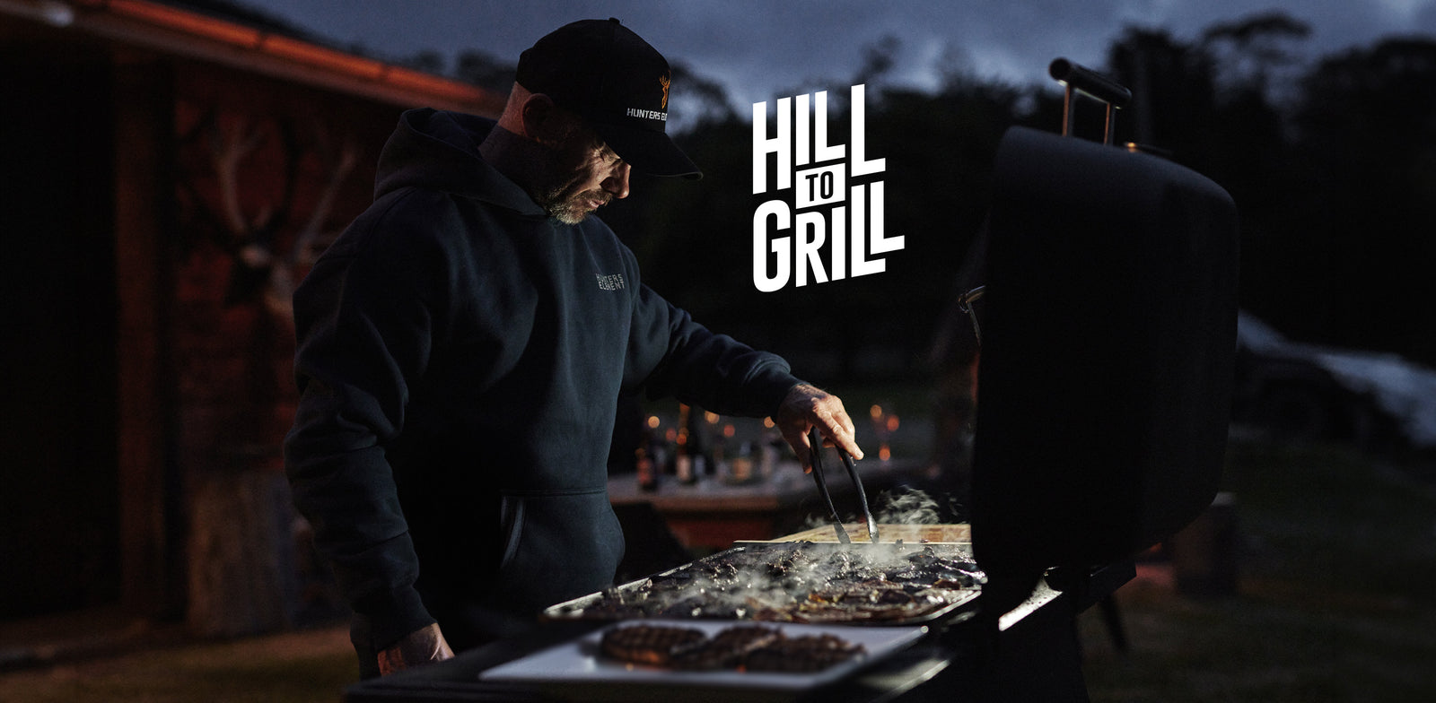 Two people grilling outdoors at night with 'Hill to Grill' logo.