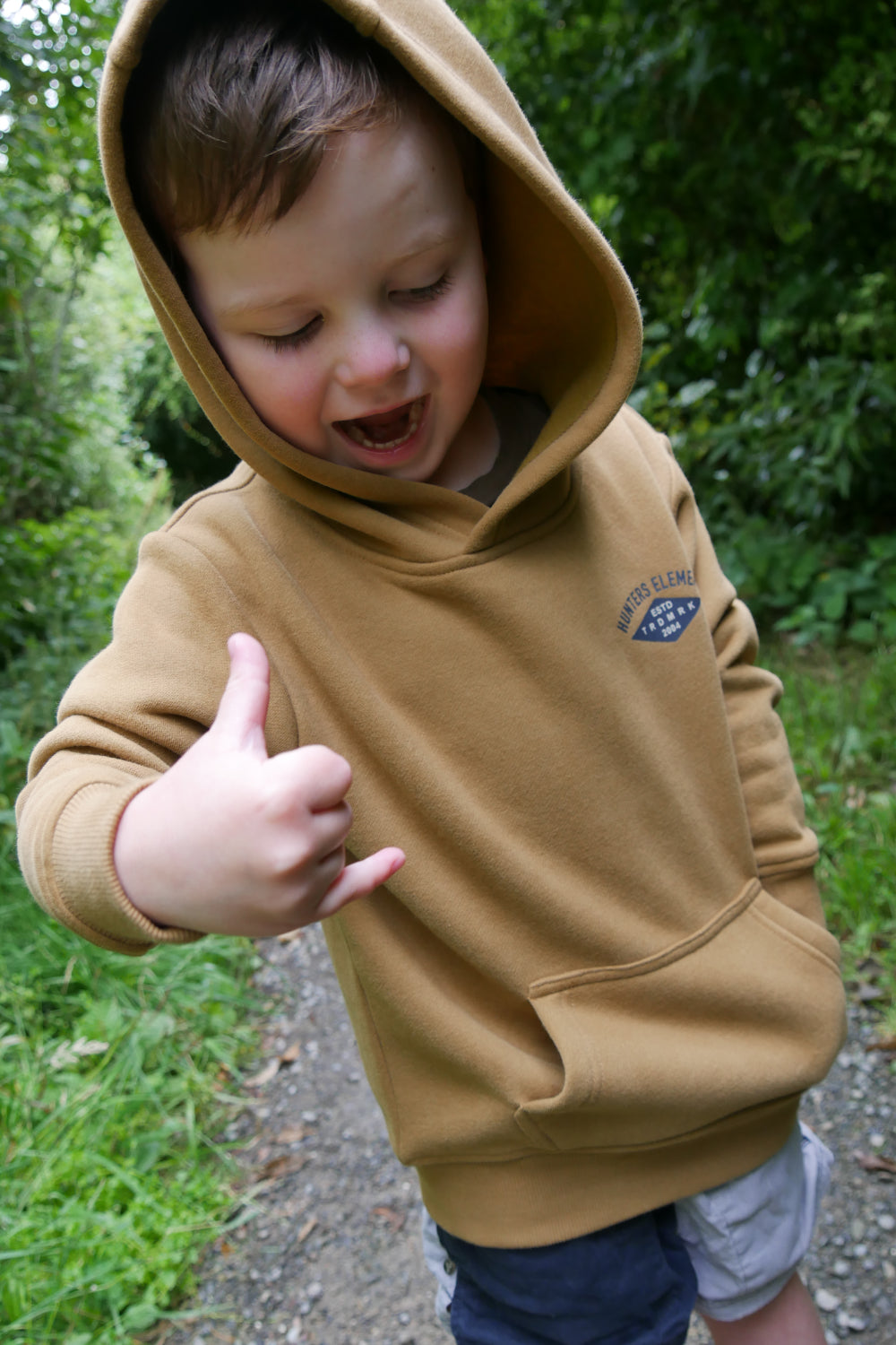 Child wearing a brown hoodie outdoors with greenery in the background